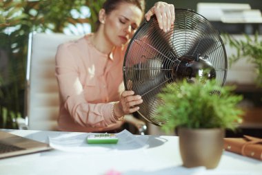 Sürdürülebilir iş yeri. Modern orta yaşlı muhasebeci kadın elektrikli vantilatörle çalışıyor yaz sıcağından muzdarip.
