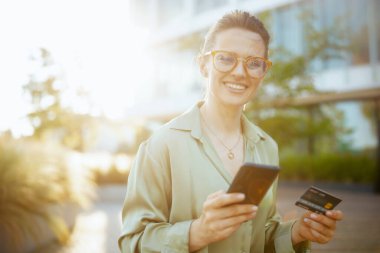 Yeşil bluzlu ve gözlüklü, akıllı telefon kullanan gülümseyen modern kadın işçiler..