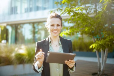 Gülümseyen 40 yaşında, iş merkezinin yakınında tabletli siyah ceketli bir kadın..