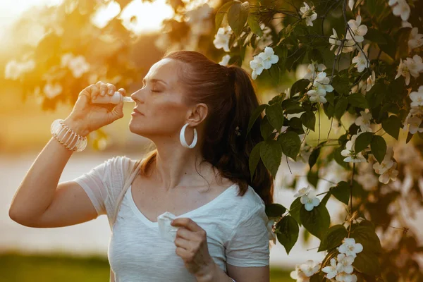 夏天的时候穿着白衬衫 穿着时髦的40岁妇女在开花树附近喷鼻水 — 图库照片