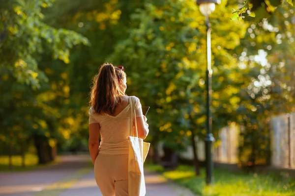 夏天的时候从后面看穿着白衬衫 头戴手提包的时髦女人走在城市公园里 — 图库照片