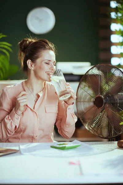 持続可能な職場 幸せな現代40歳の女性従業員と仕事で電気ファン水とレモンのカップ — ストック写真