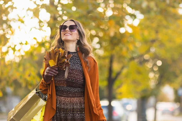 十一月 城市里快乐优雅的中年妇女 身穿棕色的战壕外套 头戴购物袋 头戴秋天的黄叶 — 图库照片
