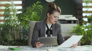 Sürdürülebilir iş yeri. Modern yeşil ofisteki gri takım elbiseli, tabletli, güler yüzlü 40 yaşında, küçük işletme sahibi bir kadının portresi..