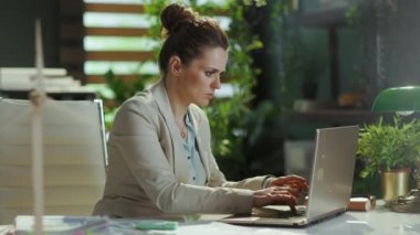 Modern yeşil ofiste hafif bir iş elbisesi içinde, dizüstü bilgisayarı olan modern kadın işçi..