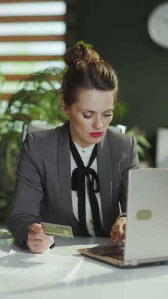 持続可能な職場 ラップトップとクレジットカードで現代のグリーンオフィスでグレーのビジネススーツを着た現代の女性労働者 — ストック動画