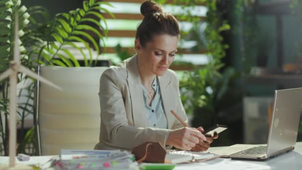现代40岁的女商人穿着轻便的西装 在现代绿色办公室里 手持笔记本电脑和笔记本电脑 用的是智能手机 — 图库视频影像
