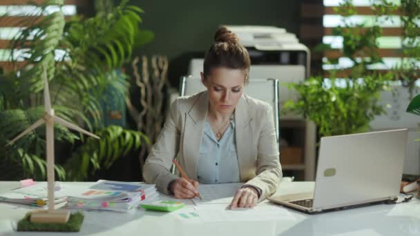 穿着轻便西服的现代小业主妇女穿着现代绿色办公室的文件和笔记本电脑 — 图库视频影像