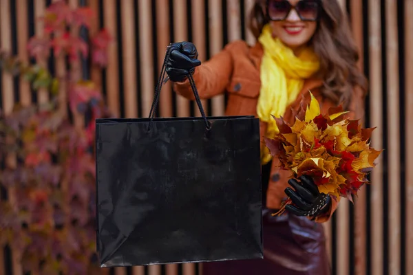 城市里穿着棕色风衣 头戴购物袋 头戴秋天黄叶的快乐的现代女人的衣服 — 图库照片