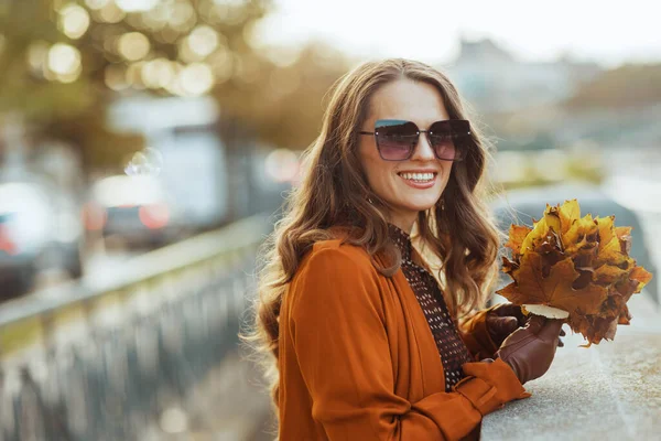 在城市里 穿着褐色风衣的现代女性微笑着 秋天是黄色的叶子 — 图库照片