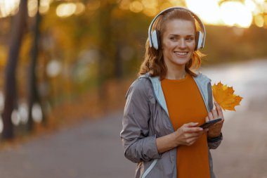 Merhaba sonbahar. Parkta sonbahar yaprağı ve kulaklıklarıyla şık giyinen mutlu bir kadın..