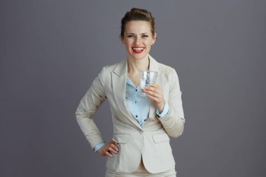 Kırk yaşında zarif bir bayan çalışan hafif bir iş elbisesi ve gri üzerinde bir bardak suyla..