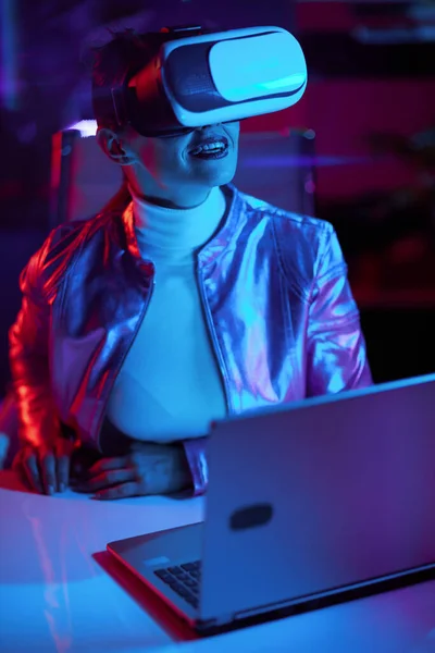 霓虹灯元的未来主义概念 现代办公室里戴着耳机的快乐的中年妇女 — 图库照片