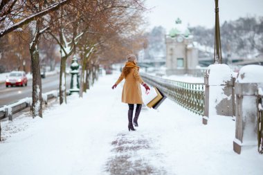 Orta yaşlı, kahverengi şapkalı, deve kürklü, eldivenli ve alışveriş çantalı mutlu bir kadın..