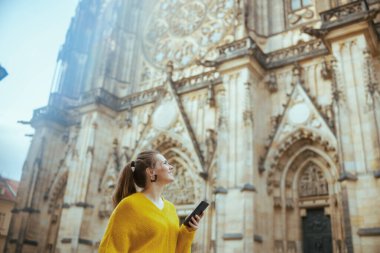 Prag Cumhuriyeti 'nde sarı bluzlu mutlu gezgin kadın akıllı telefon turu ve yürüyüşü ile.