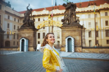 Prag Kalesi yakınlarında Prag Cumhuriyeti 'nde sarı bluz ve yağmurluk giyen güler yüzlü şık gezgin kadın..