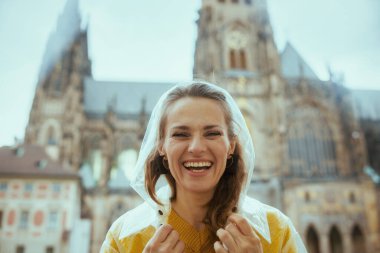 Prag 'da Çek Cumhuriyeti' nin turistik yerlerinde sarı bluz ve yağmurluk giymiş gülümseyen modern yalnız gezgin kadın portresi..