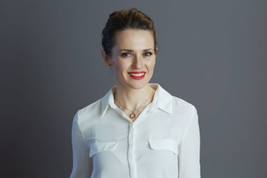 40 yaşında, beyaz bluzlu, gri arka planlı, küçük işletme sahibi bir kadın..