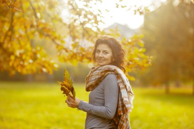 Merhaba sonbahar. 40 yaşındaki mutlu bir kadının sonbahar yaprakları ve eşarplarıyla parktaki portresi..