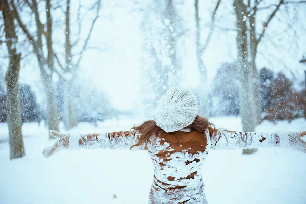 冬に街の外で雪をキャッチミトンで雪の服と羊皮のコートで茶色の帽子とスカーフの女性の後ろから見た — ストック写真