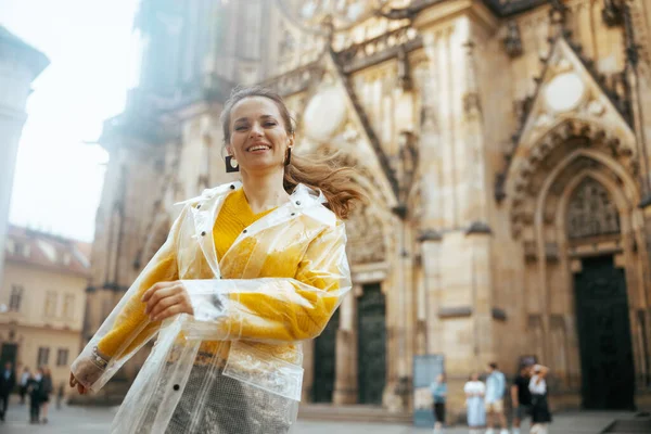 在布拉格 穿着黄色衬衫和雨衣的中年妇女兴高采烈地走在人行道上 — 图库照片