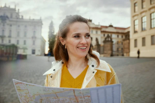 布拉格城堡附近穿着黄色上衣和雨衣 头戴地图的快乐的年轻单身女性 — 图库照片