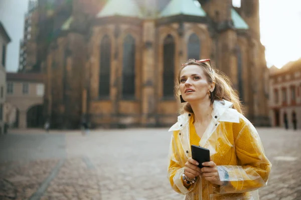 在布拉格 穿着黄色上衣和雨衣的现代女性游客们惊愕不已 她们一边散步一边用的是智能手机 — 图库照片