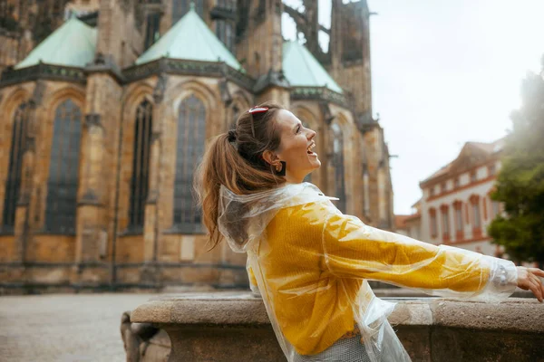 在布拉格 穿着黄色衬衫和雨衣的快乐的现代女性正在探索各种吸引人的地方 — 图库照片