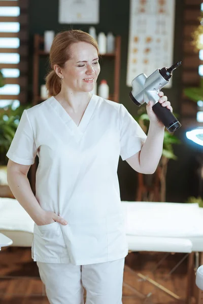 卫生保健时间 快乐的女按摩师在温泉沙龙用按摩枪按摩 — 图库照片