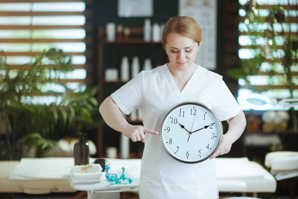 Healthcare time. female massage therapist in spa salon with clock.