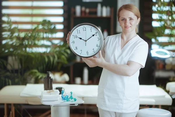Healthcare time. female massage therapist in spa salon with clock.