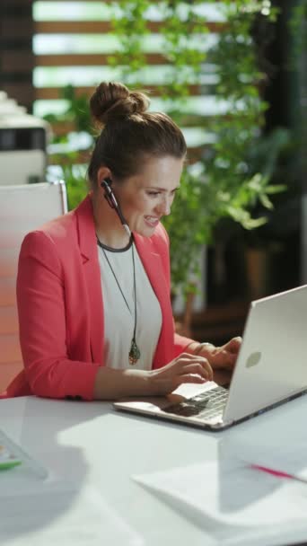 可持续工作场所 快乐的现代小企业主女人穿着红色夹克 头戴耳机和笔记本电脑上班 — 图库视频影像