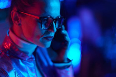 Neon metaevren fütüristik konsepti. Gözlüklü moda kadın akıllı telefondan konuşuyor..