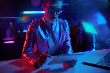Neon metaevren fütüristik konsepti. Modern ofiste tablet bilgisayar kullanan gözlüklü zarif iş kadını..