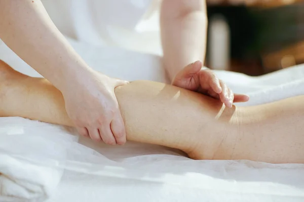 Healthcare time. Closeup on massage therapist in spa salon massaging clients leg on massage table.