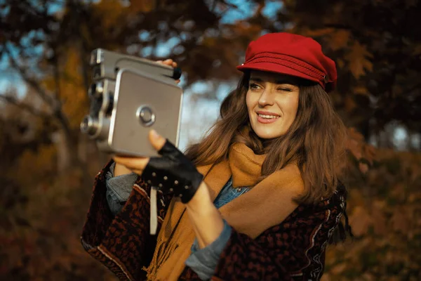 Hello autumn. stylish female in red hat with retro video camera, scarf and gloves in the city park.