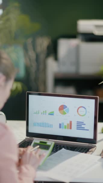 現代のオフィスでチャートで働く電卓とラップトップを持つ現代の女性の後ろから見た — ストック動画