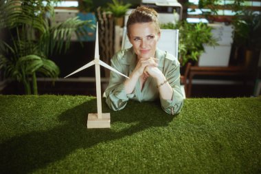 Eko zamanı. Yeşil bluzlu 40 yaşındaki iş kadını, modern yeşil ofisinde yel değirmeni kullanıyor.