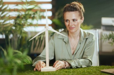 Çevre trendleri. Orta yaşlı iş kadını yeşil bluzlu modern yeşil ofiste yel değirmeni ile