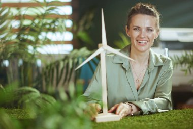 Eko işi. Yeşil bluzlu, mutlu, küçük işletme sahibi kadın yel değirmenli modern yeşil ofiste.