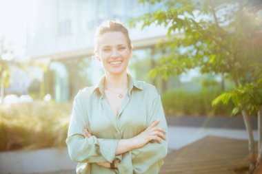 Orta yaşlı, mutlu bir iş kadını portresi. İş merkezine yakın, yeşil bluzlu, kollarını kavuşturmuş..