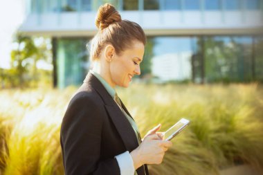 gülümseyen modern kadın işçi iş merkezinin yanında siyah ceketli tablet bilgisayar kullanıyor..