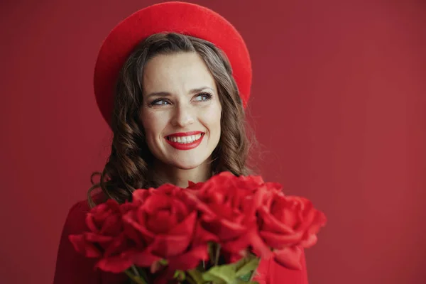 ハッピーバレンタイン 赤いバラの赤い背景に対して赤いドレスとベレーのスタイリッシュな40歳の女性の肖像画 — ストック写真