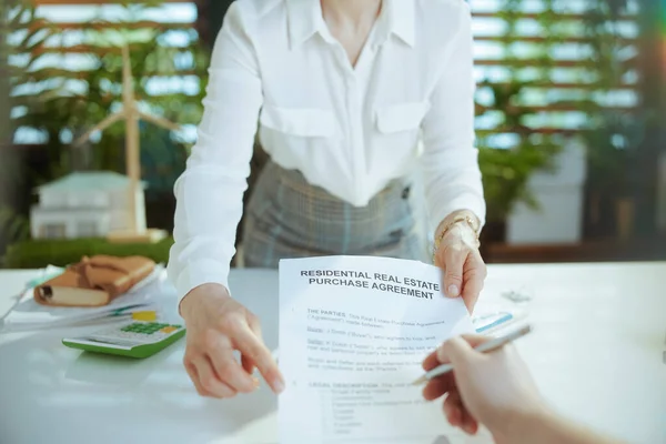 Sustainable real estate business. Closeup on middle aged business woman in modern green office in white blouse with calculator, document and client.