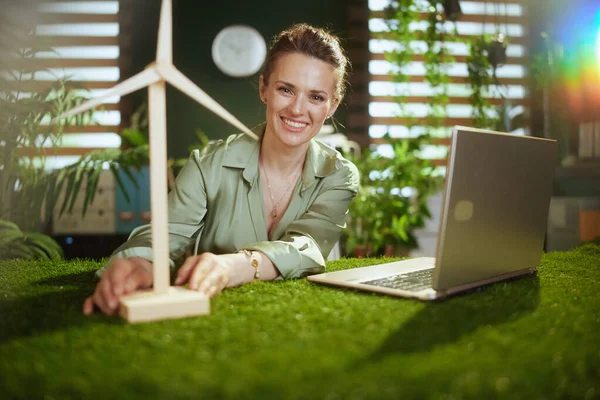 smiling 40 years old business woman in green blouse in modern green office with laptop and windmill