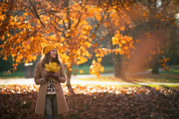 こんにちは 11月 秋の市立公園で秋の黄色の葉とベージュコートとオレンジの帽子のペンシブトレンディな女性 — ストック写真