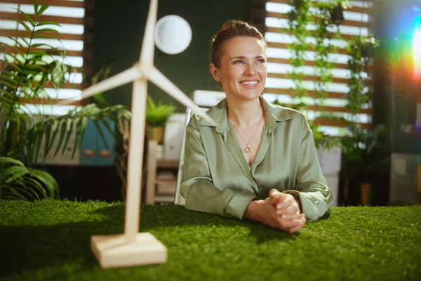 生态趋势 时尚的中年小企业主女人穿着绿色衬衫 穿着现代绿色办公室的风车 图库照片