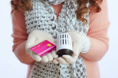 Merhaba kış. Modern orta yaşlı kadın, kazak, eldiven, şapka ve atkı, soba sapı ve kredi kartı, beyaza izole edilmiş..