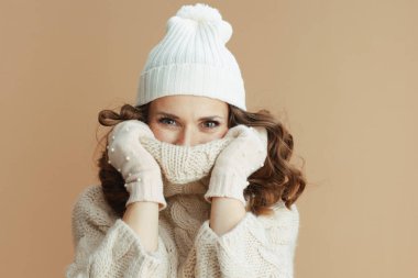 Merhaba kış. Bej kazaklı, eldivenli ve yakasına sarılmış bej arka planda izole edilmiş orta yaşlı zarif bir kadın..