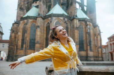 Prag Çek Cumhuriyeti 'nde sarı bluz ve yağmurlukla gezintiye çıkan şık, şık, yalnız bir turist kadın..